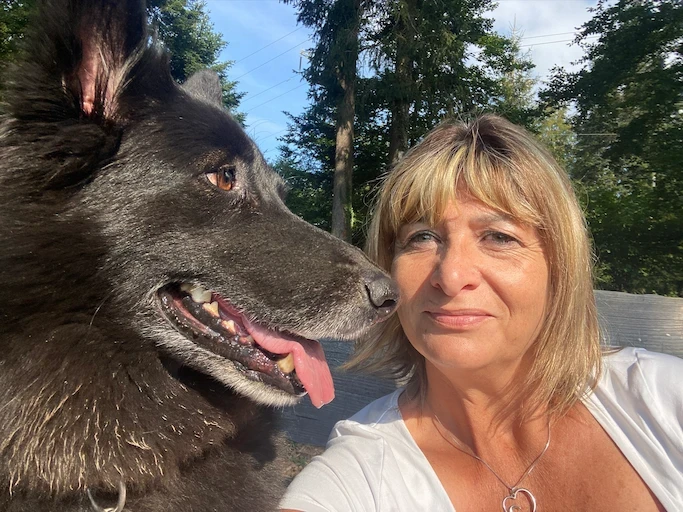 Fabienne en extérieur, joue contre joue avec un grand chien noir